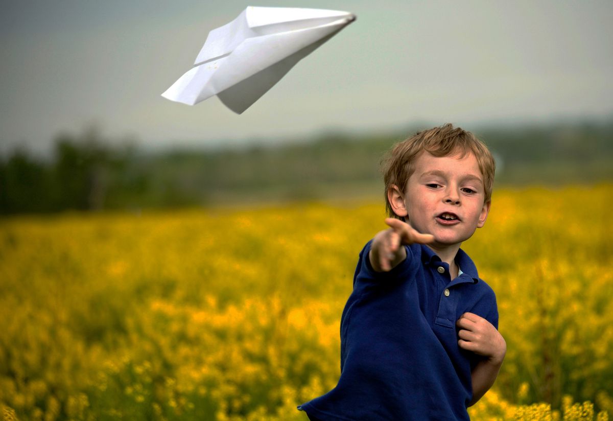 A boy throwing a paper airplane outside